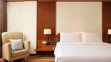 A hotel room with a bed, a chair, a nightstand, and a wall panel.