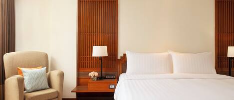A hotel room with a bed, a chair, a nightstand, and a wall panel.