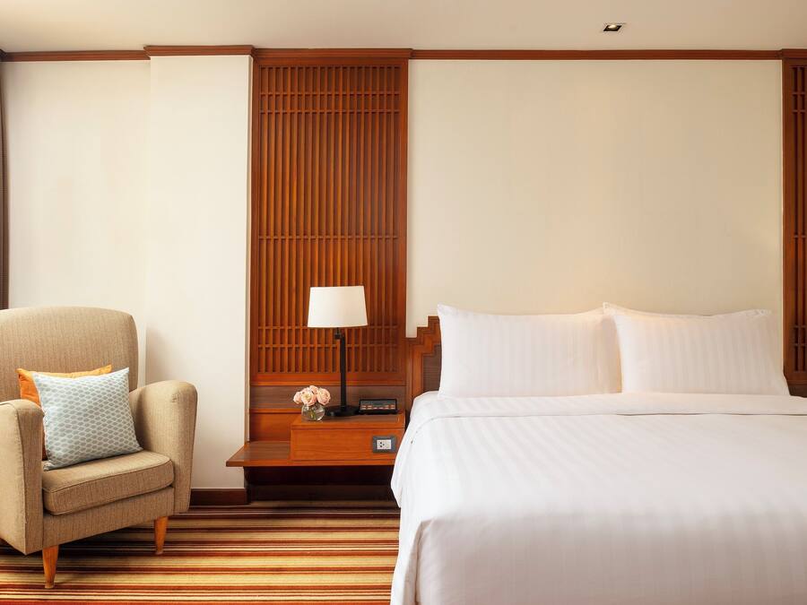 A hotel room with a bed, a chair, a nightstand, and a wall panel.