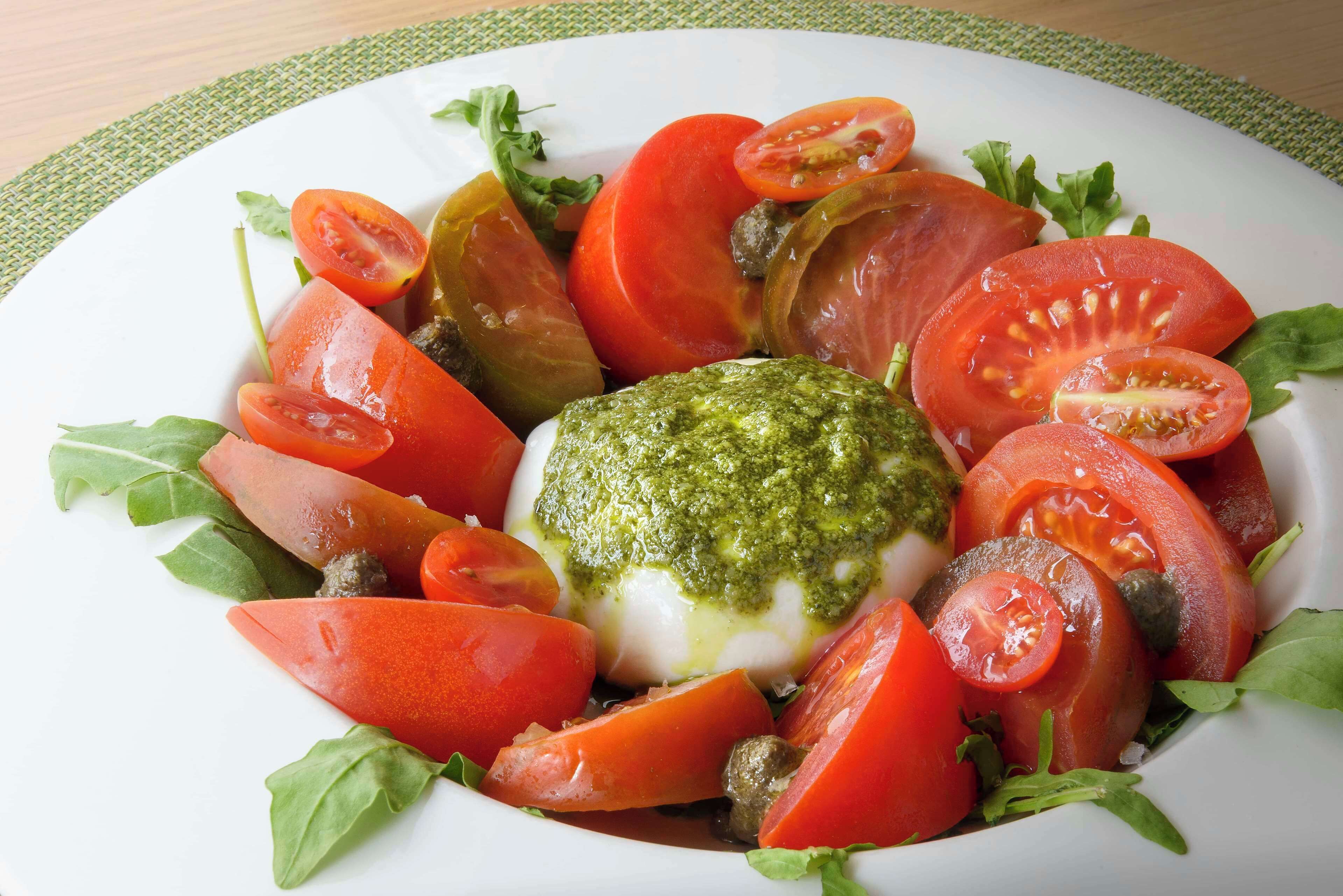 A plate of food with tomatoes, basil, and a green sauce.