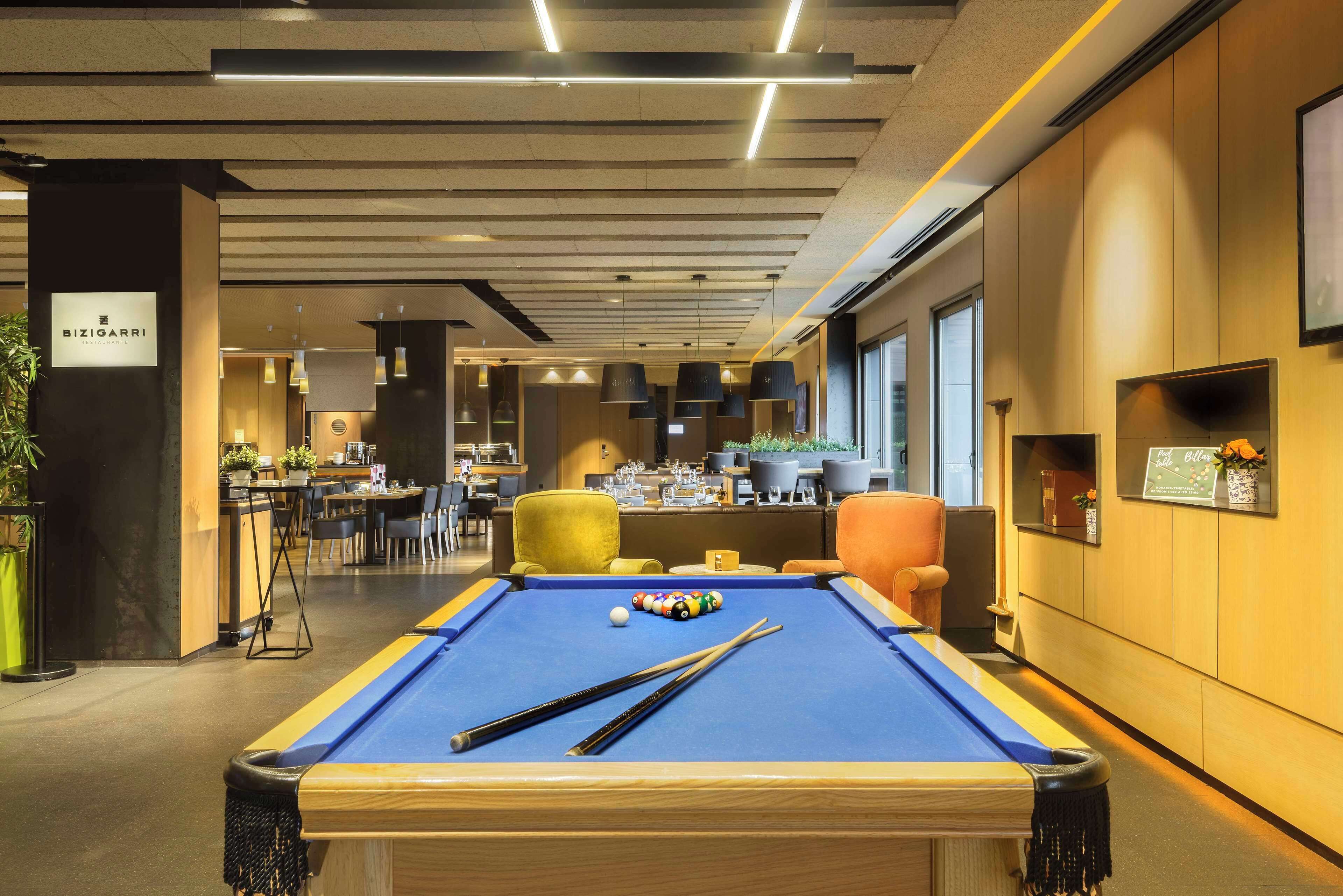 A pool table with pool cues and balls, a bar area with seating, and a sign for 'BIZIGARRI'.