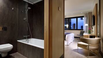 Un bagno moderno con doccia vetro, vasca e WC. Nella stanza adiacente, un letto con scrivania e sedia.