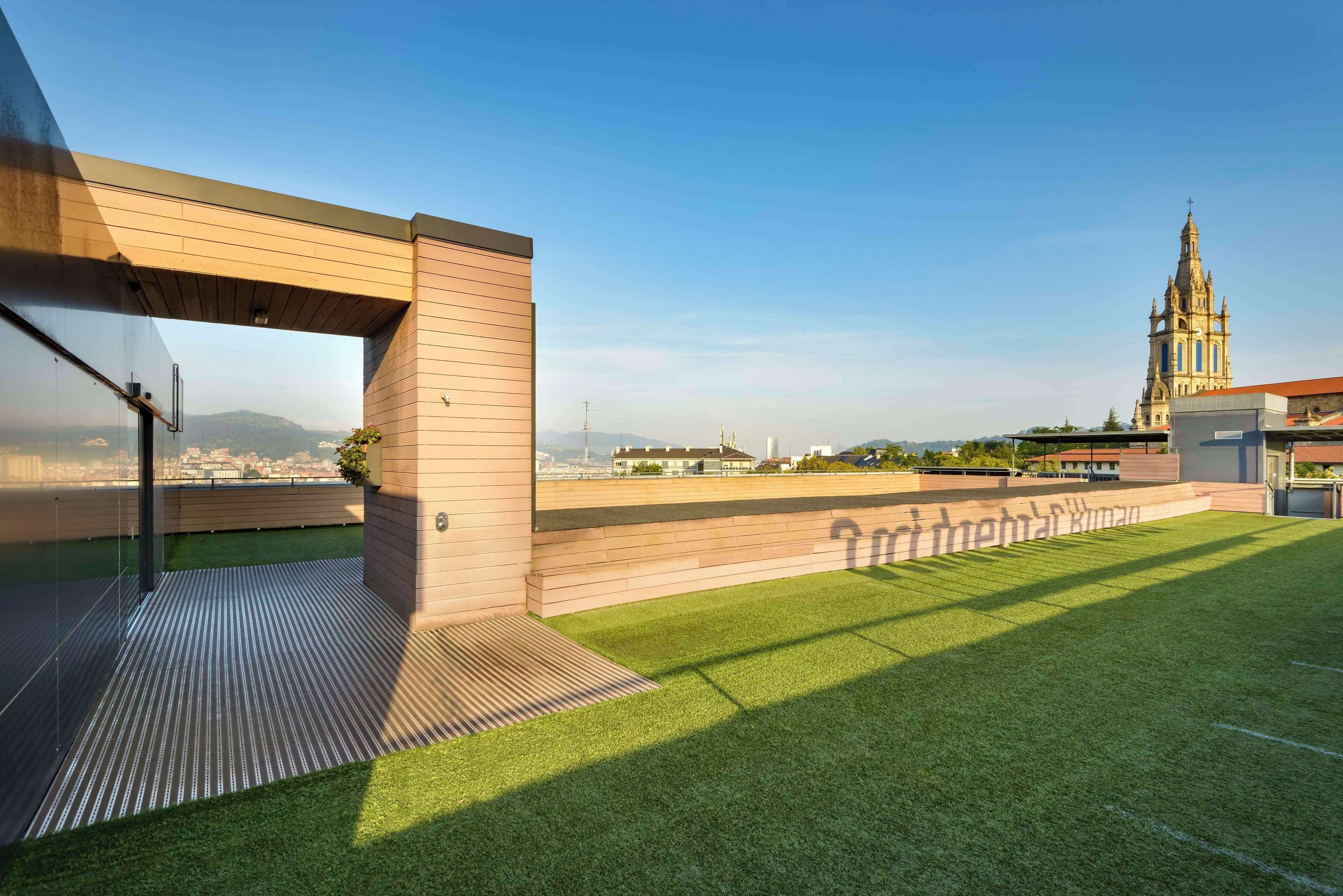 A modern building with a rooftop terrace featuring artificial grass and a wooden deck.