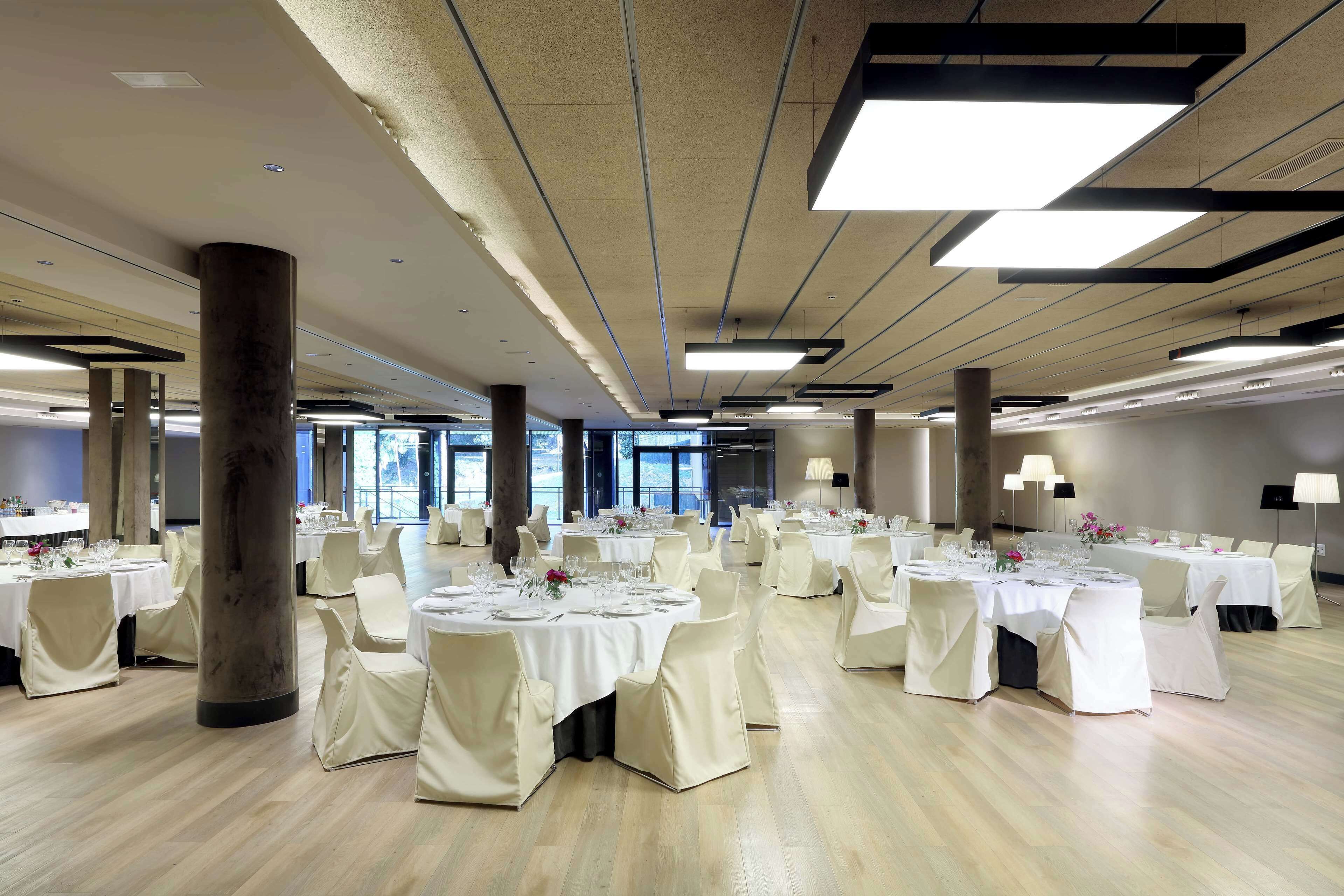 A spacious banquet hall with round tables set for dining, large pillars, and modern lighting fixtures.
