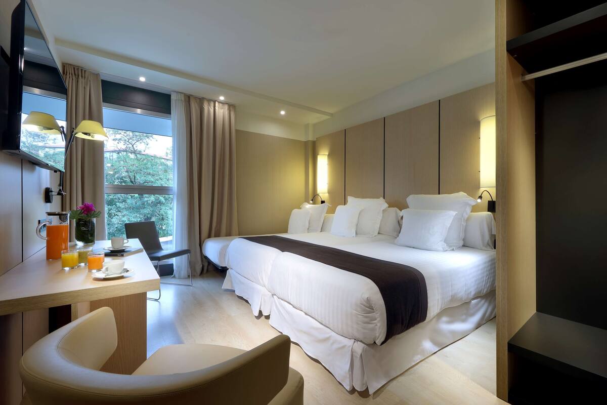 A modern hotel room with a large bed, a desk with a chair, and a view of the outdoors.