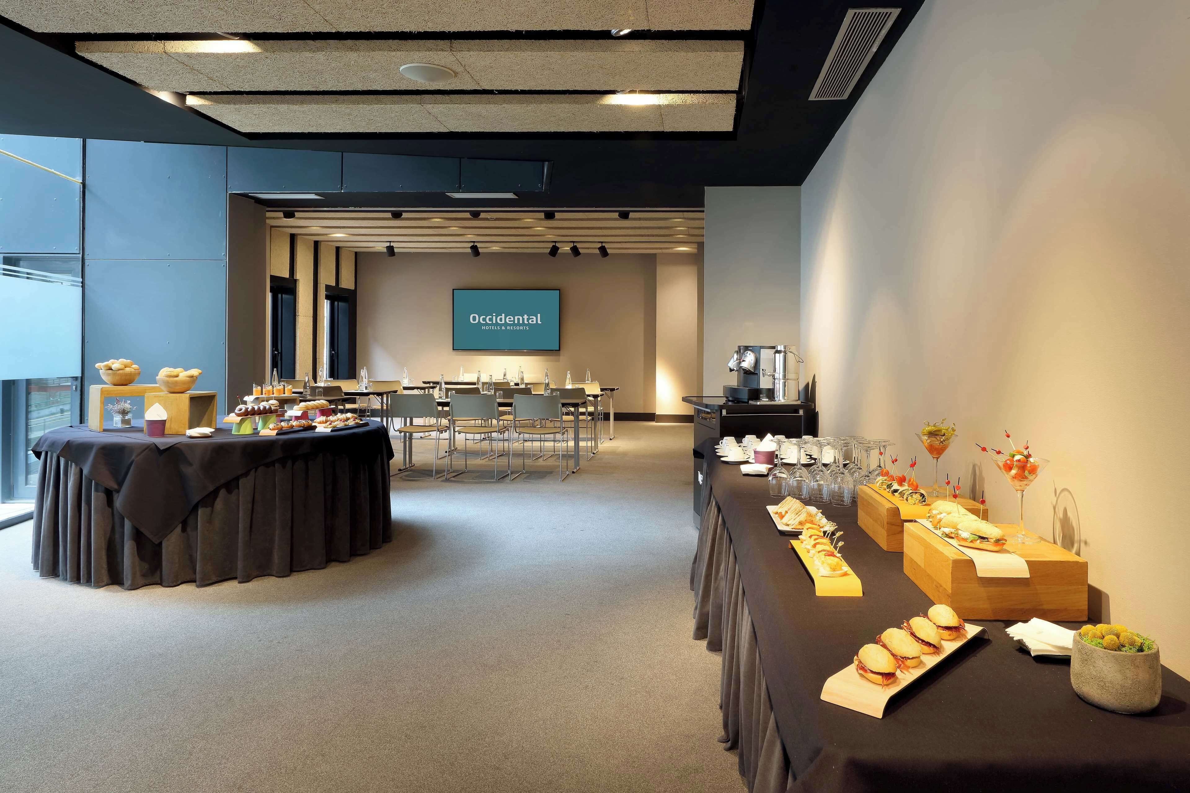 Une salle de conférence avec une longue table dressée pour un buffet, un écran de projection affichant le logo « Occidental Hotel & Resorts », et un espace détente avec des chaises.