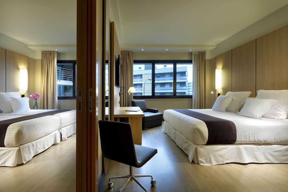 A hotel room with two beds, a desk, and a chair.