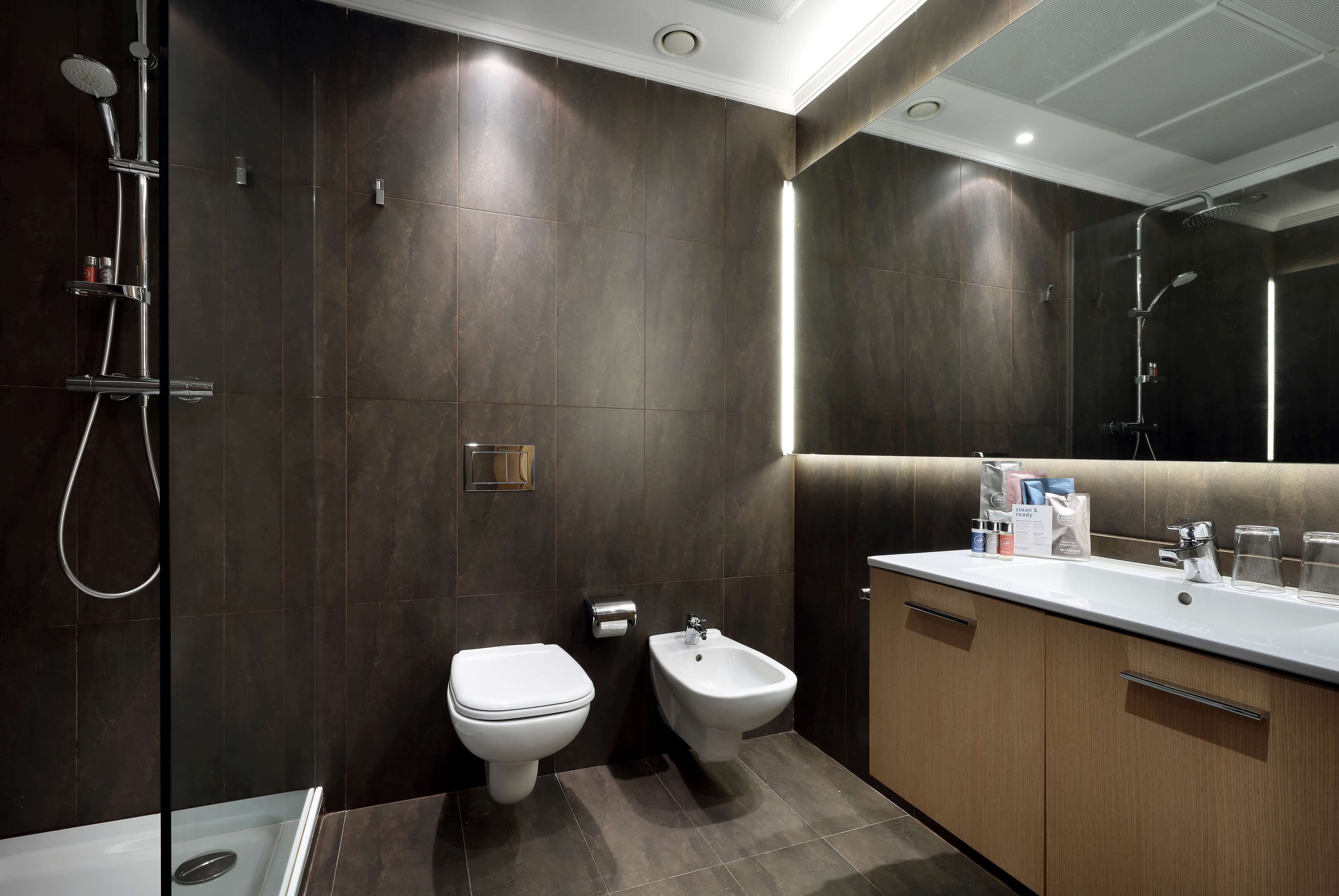 Ein modernes Badezimmer mit Dusche, Toilette, Bidet und einem Waschtisch mit Spiegel und Waschbecken.