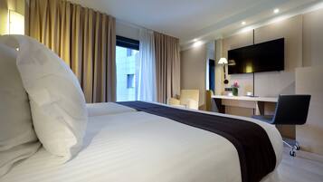 A hotel room with a large bed, a desk with a chair, a TV, and a window with curtains.
