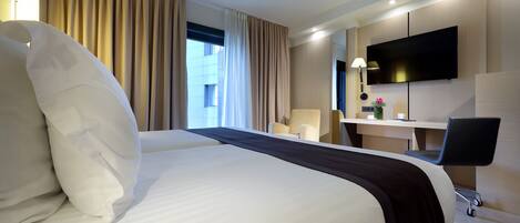 Ein Hotelzimmer mit einem großen Bett, einem Schreibtisch mit Stuhl, einem Fernseher und einem Fenster mit Vorhängen.
