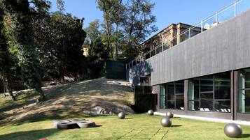 Un edificio moderno con grandes ventanales, un área verde con equipamiento de ejercicio y árboles al fondo.