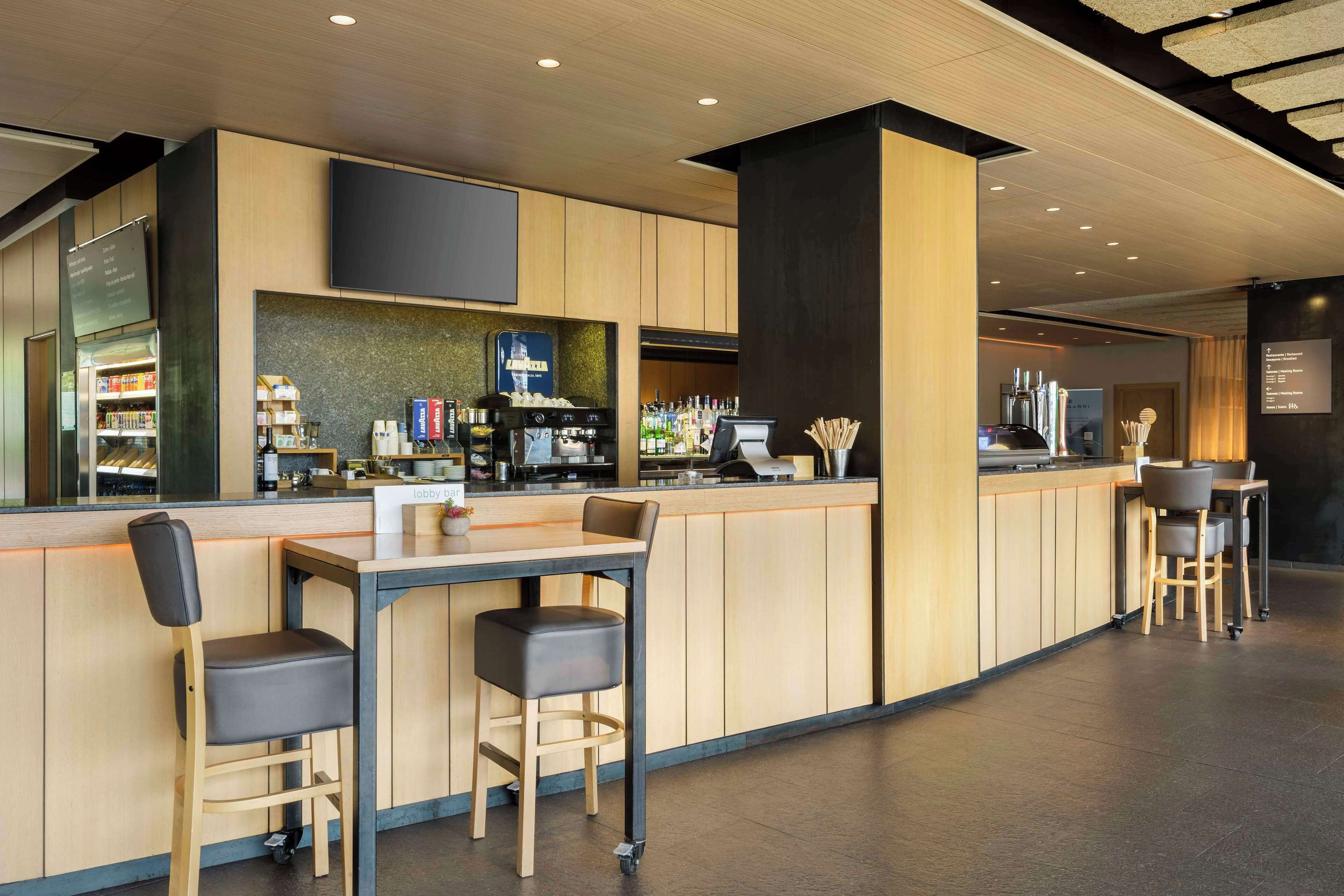Un área de bar moderna con mostrador, taburetes y una variedad de bebidas y aperitivos.