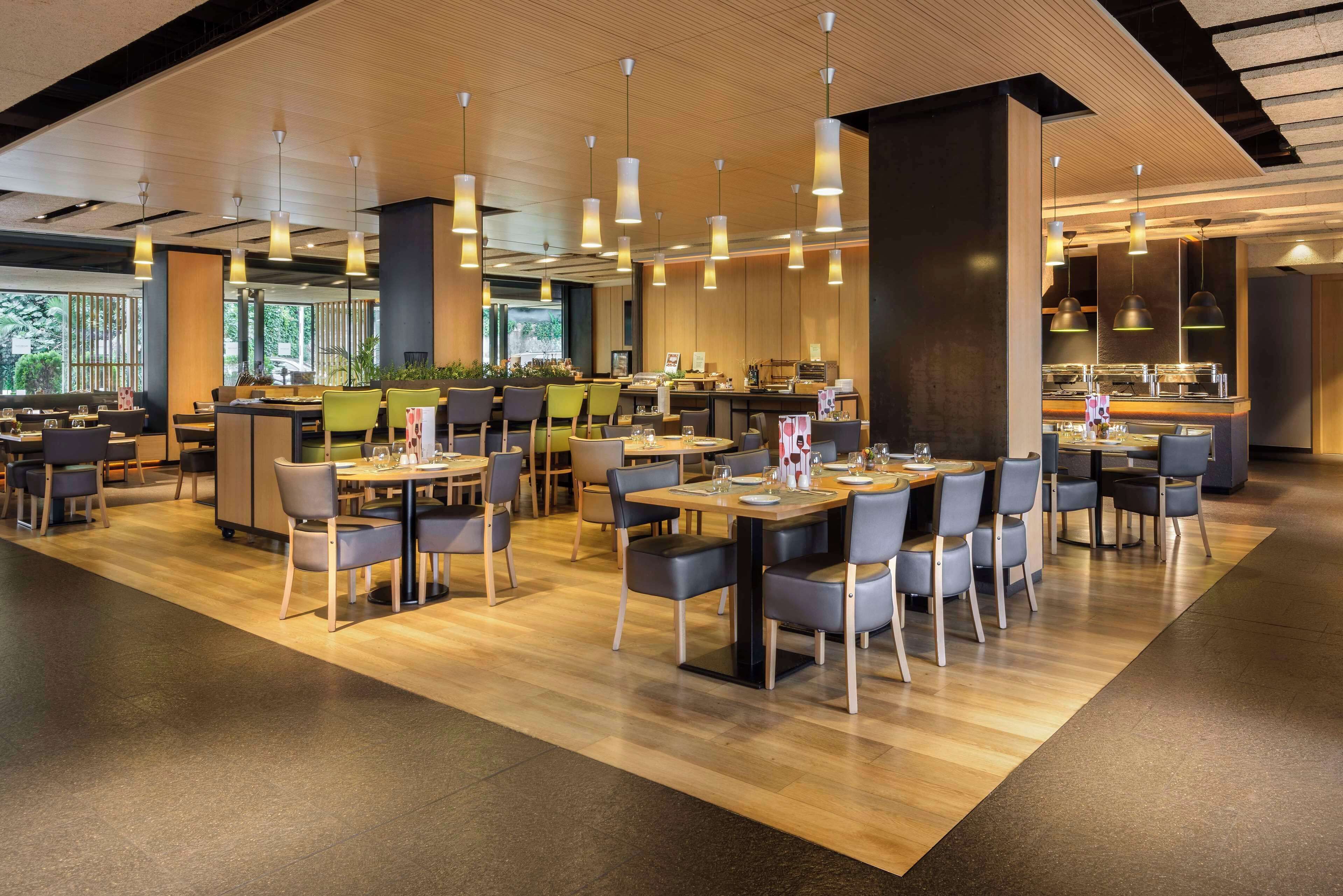 Un restaurante moderno con varias zonas de comedor, suelo de madera e iluminación colgante.