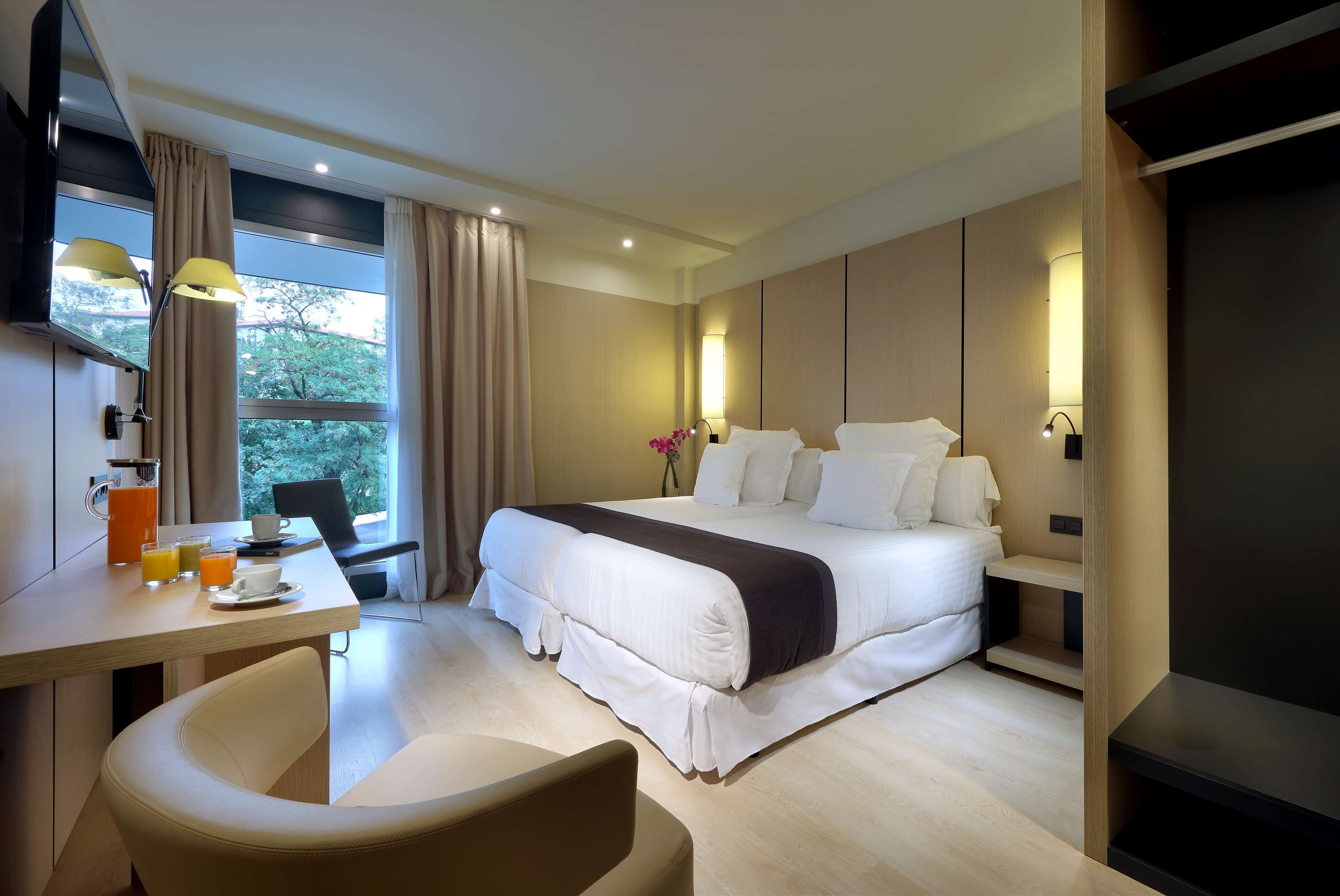 Habitación de hotel moderna con una cama grande, un escritorio con silla, un televisor y una ventana con cortinas.