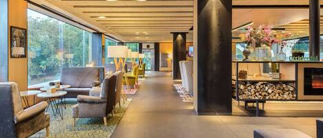 A modern lobby with seating areas, a fireplace, and a large window offering a view of greenery.