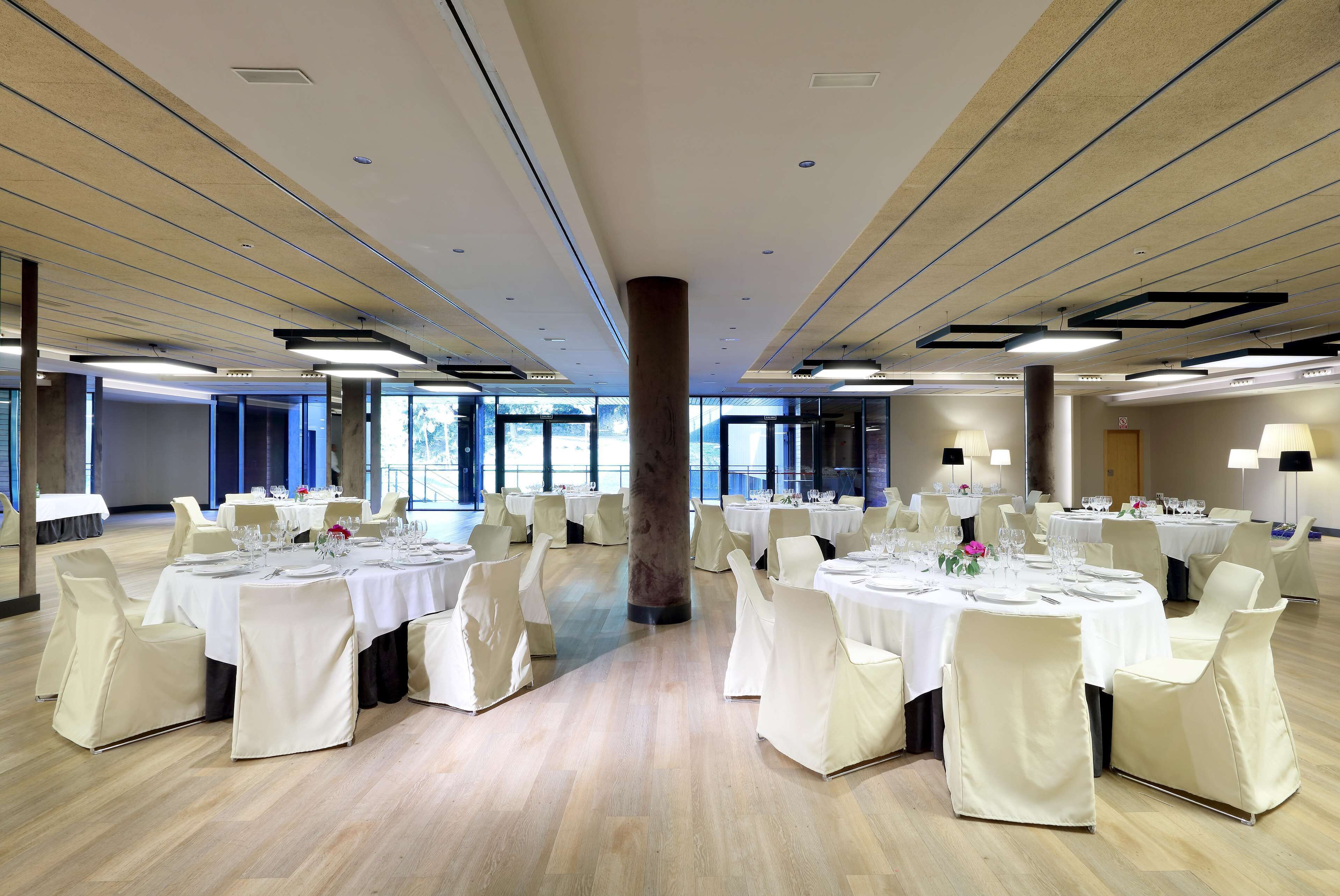 A spacious banquet hall with multiple round tables set for dining, each with white tablecloths and chairs.