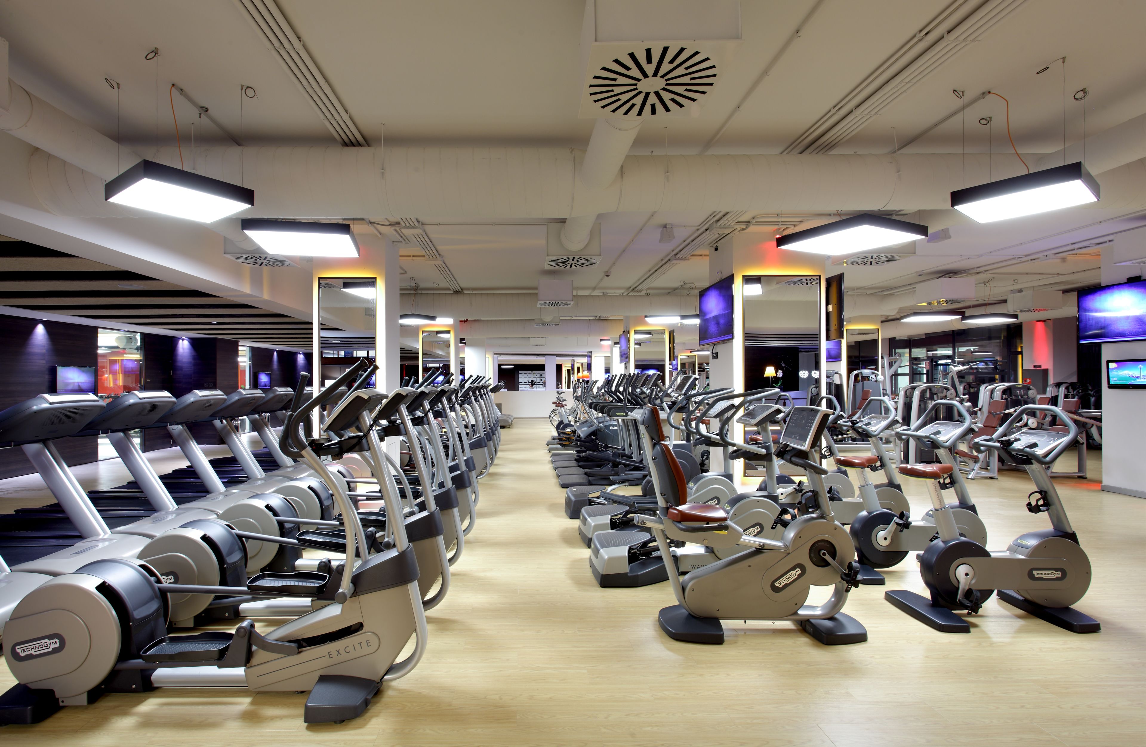 Un gimnasio con varias máquinas de ejercicio, incluyendo cintas de correr y bicicletas estáticas, dispuestas en filas.