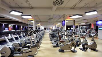 Un gimnasio con varias máquinas de ejercicio, incluyendo cintas de correr y bicicletas estáticas, dispuestas en filas.