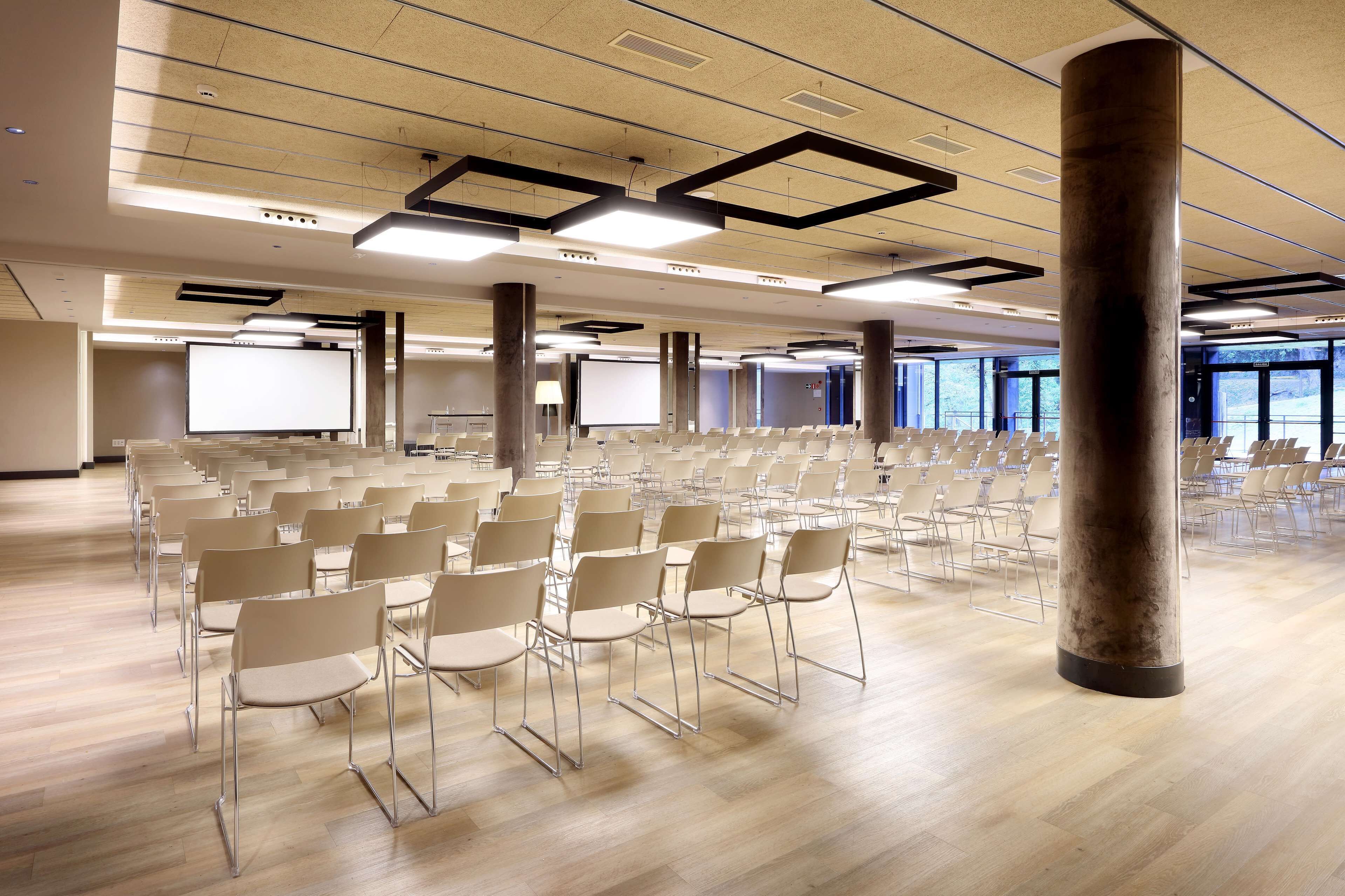 A conference room with rows of chairs, a large screen, and a pillar.