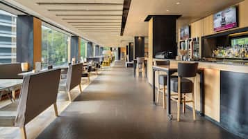 Un espace bar moderne avec un long comptoir, des tabourets de bar et un écran de télévision.