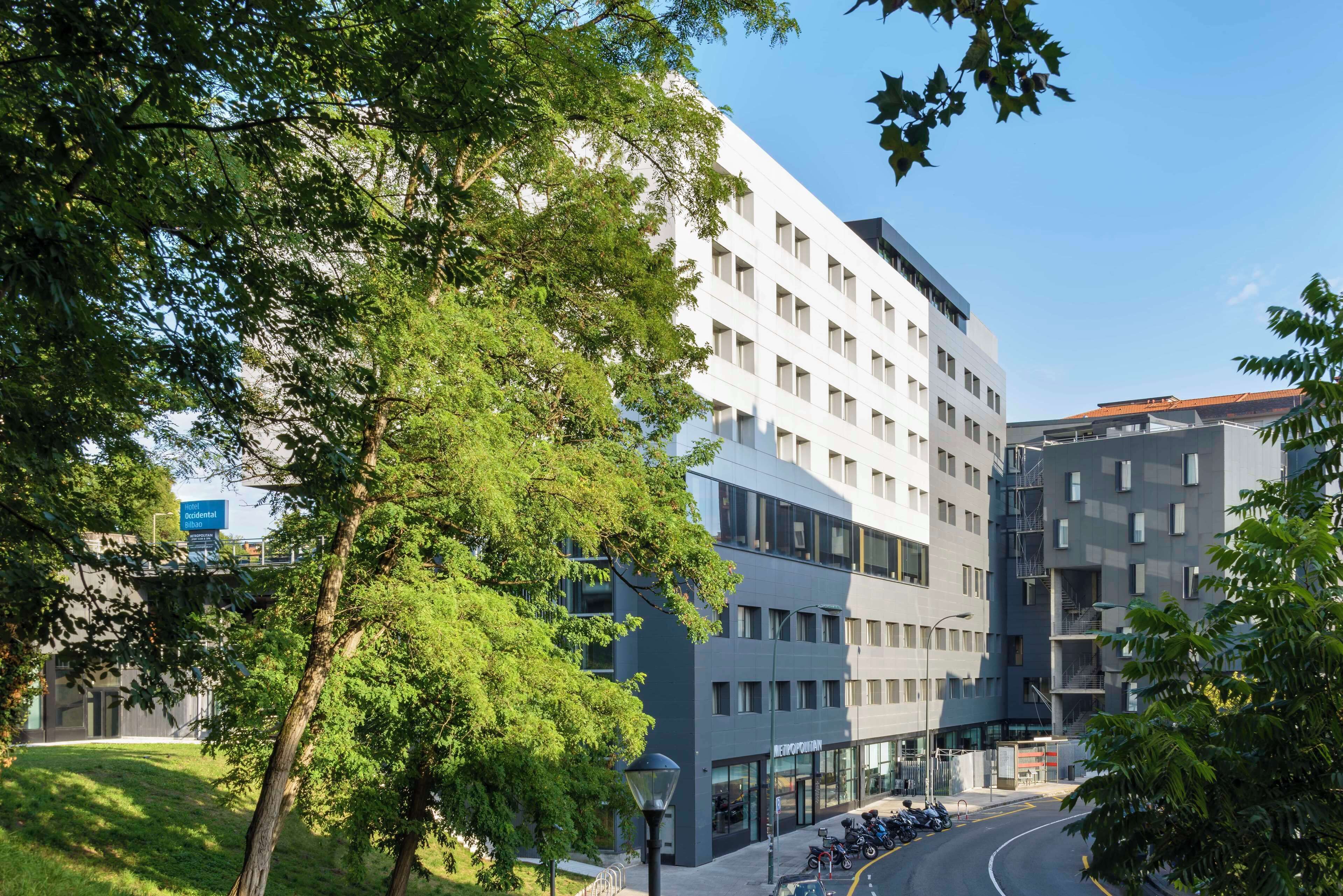 A modern building with a glass facade, surrounded by trees and a clear sky.
