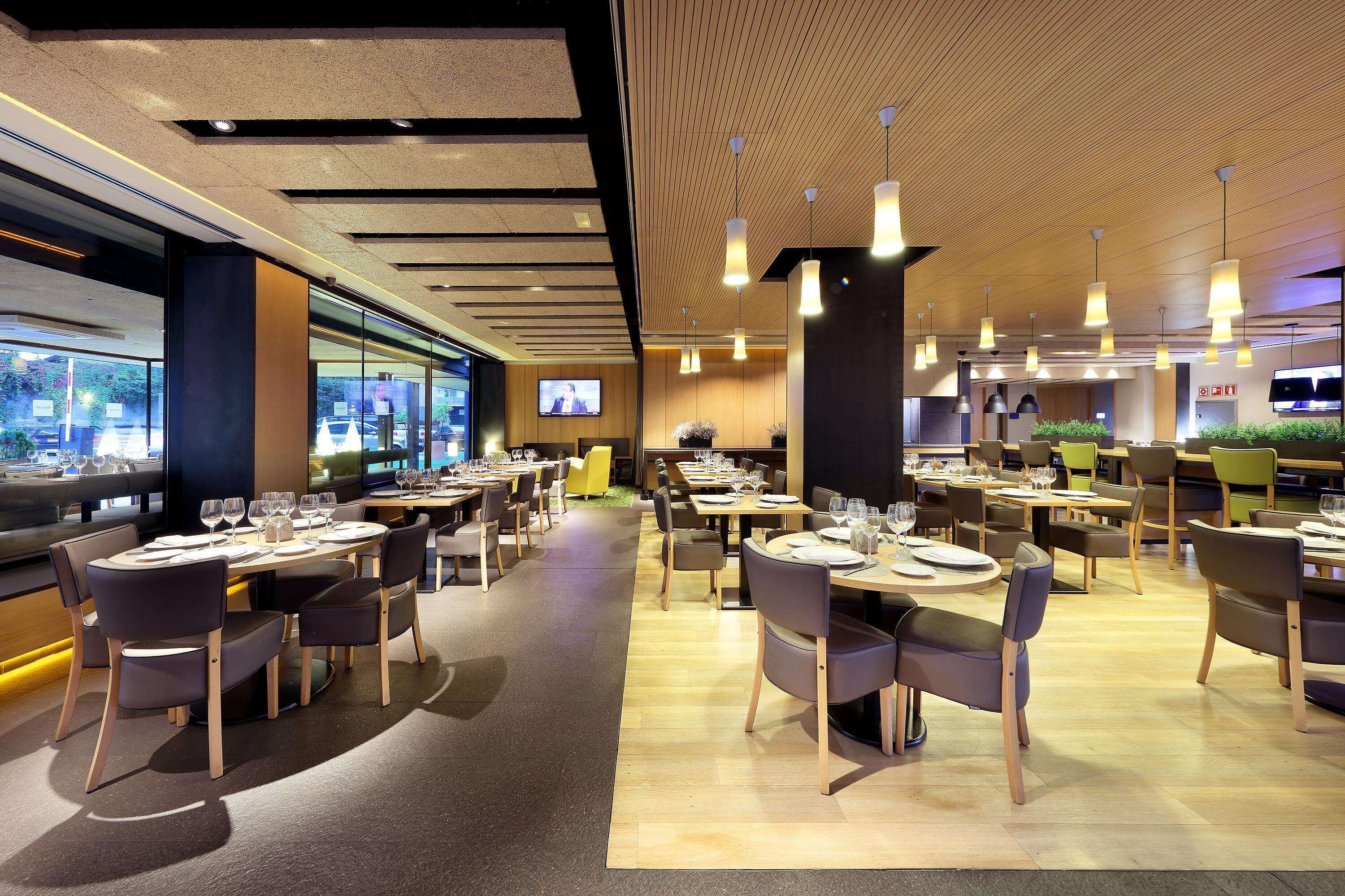 Un restaurant moderne doté de nombreuses tables et chaises, d’un plafond en bois et de grandes fenêtres.