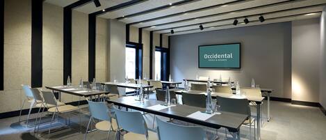 A conference room with tables and chairs, a large screen displaying "Occidental Hotels & Resorts", and a modern ceiling design.