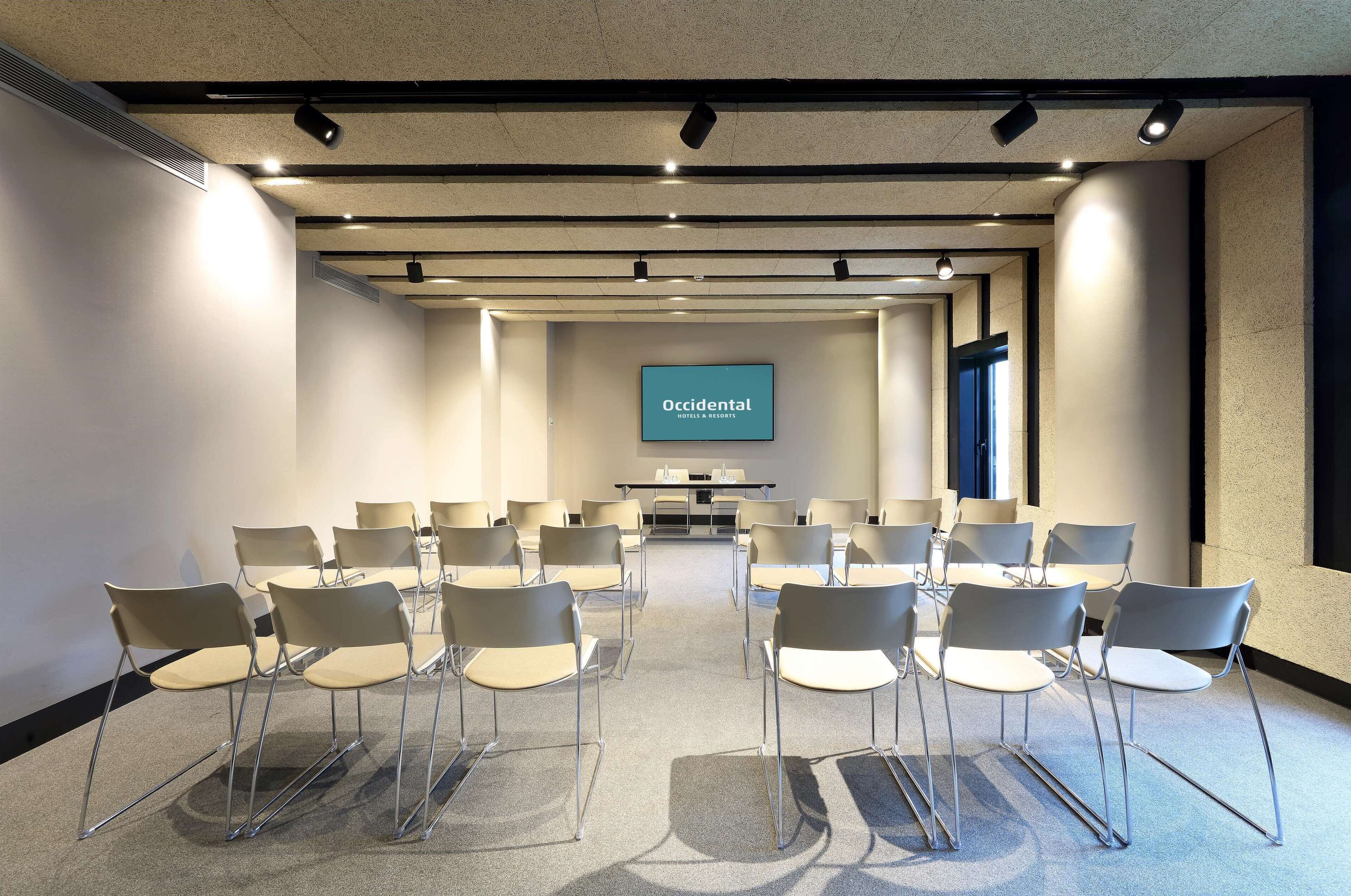 Une salle de conférence dotée d’un grand écran affichant le logo « Occidental Hotels & Resorts » et de rangées de chaises disposées pour une réunion.