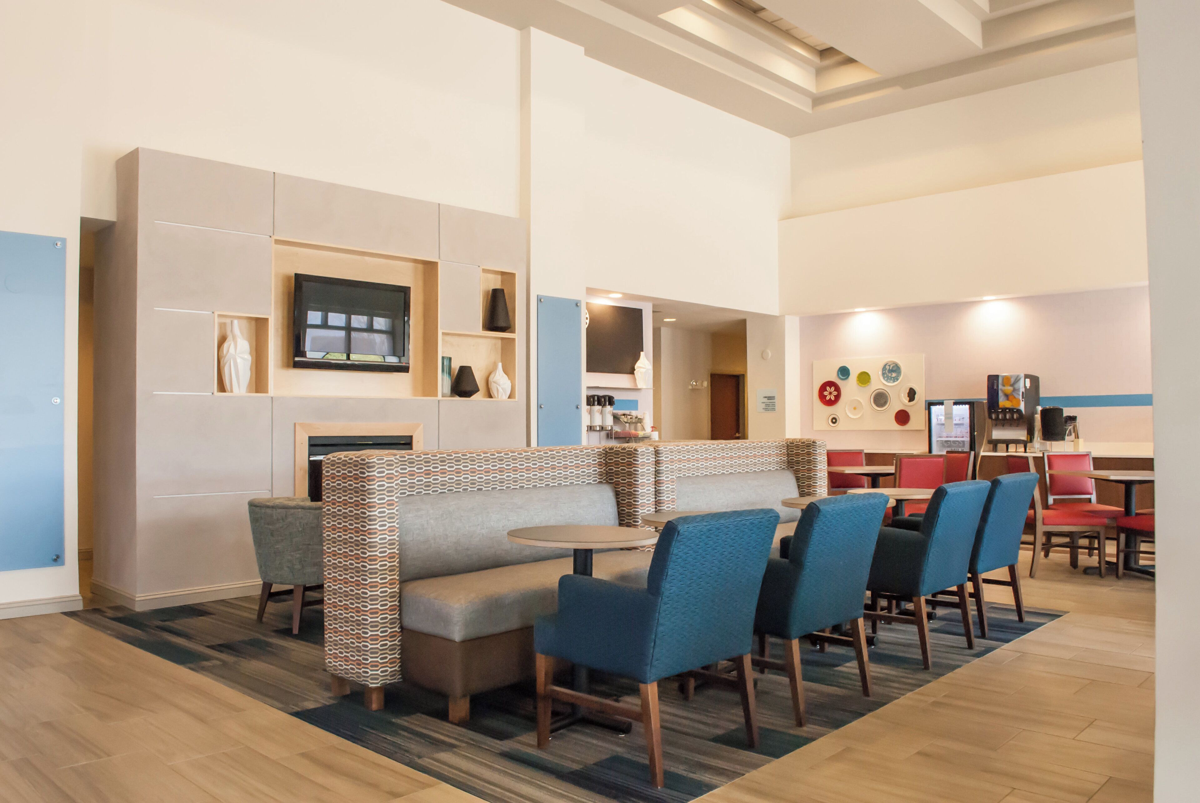 A modern hotel lobby with a seating area, a fireplace, and a television mounted on the wall.