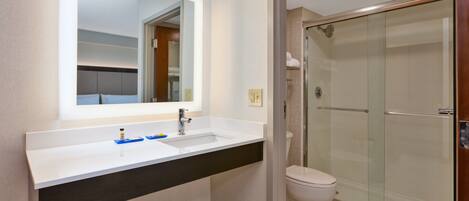 A modern bathroom with a white sink, mirror, and glass shower enclosure.