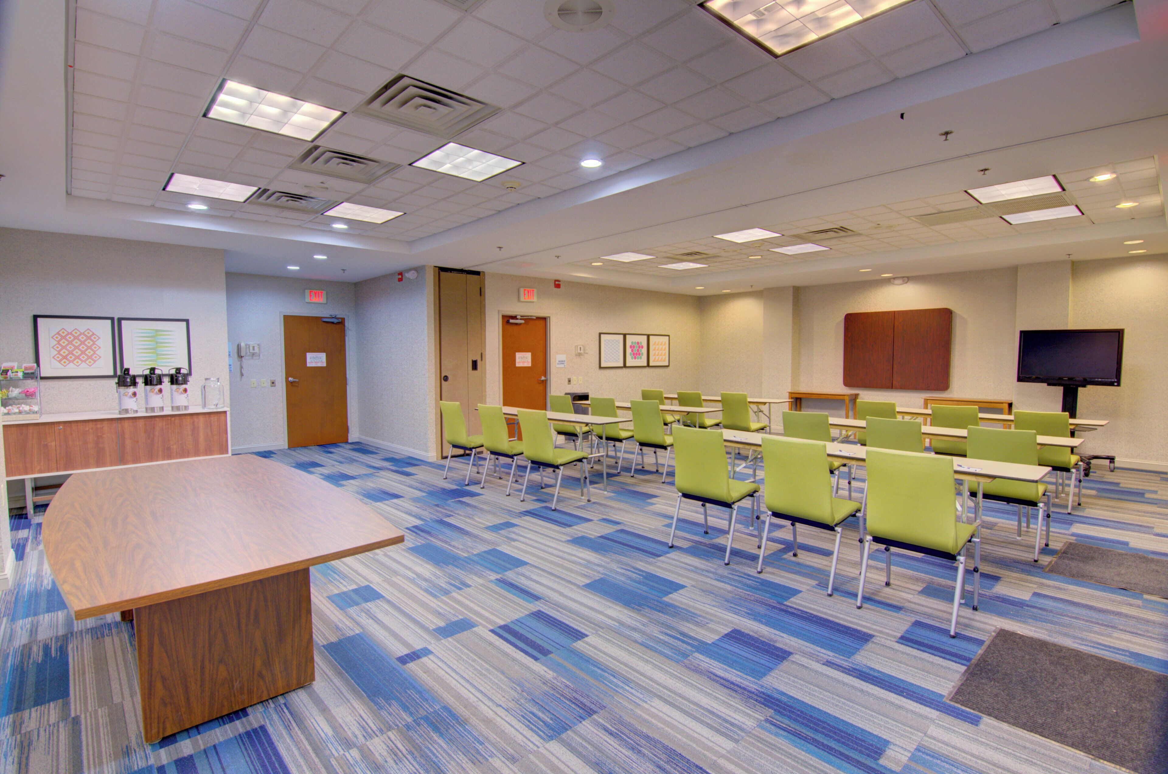 A conference room with a long table, multiple chairs, a television, and exit signs on the walls.