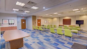 A conference room with a long table, multiple chairs, a television, and exit signs on the walls.
