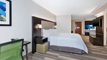 A hotel room with a bed, bedside table, chair, and a small kitchenette area.