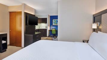 Habitación de hotel con cama, escritorio, televisor, lámpara de escritorio y baño con lavamanos y espejo.