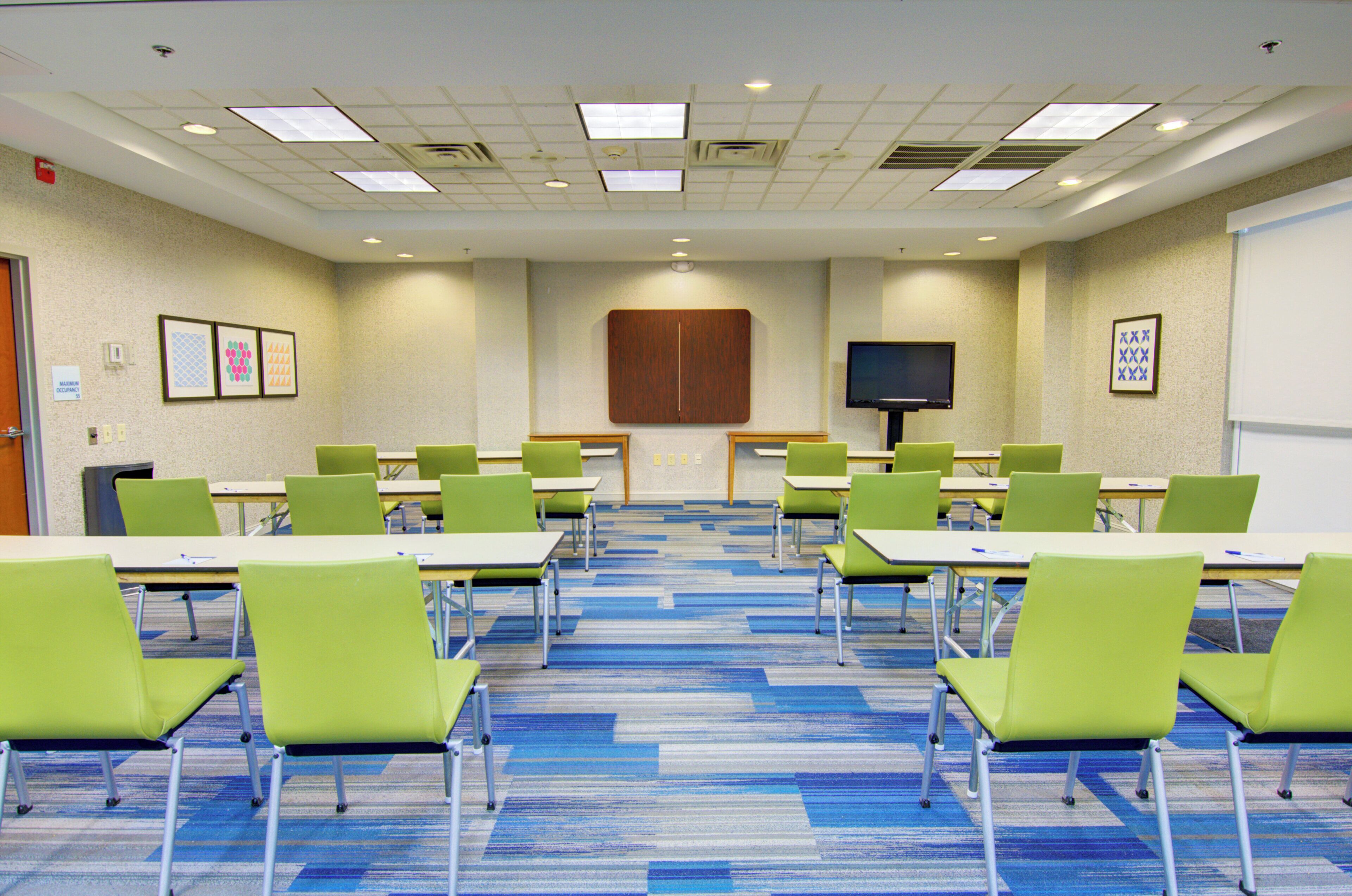 A conference room with tables and chairs, a flat-screen TV, and a whiteboard.