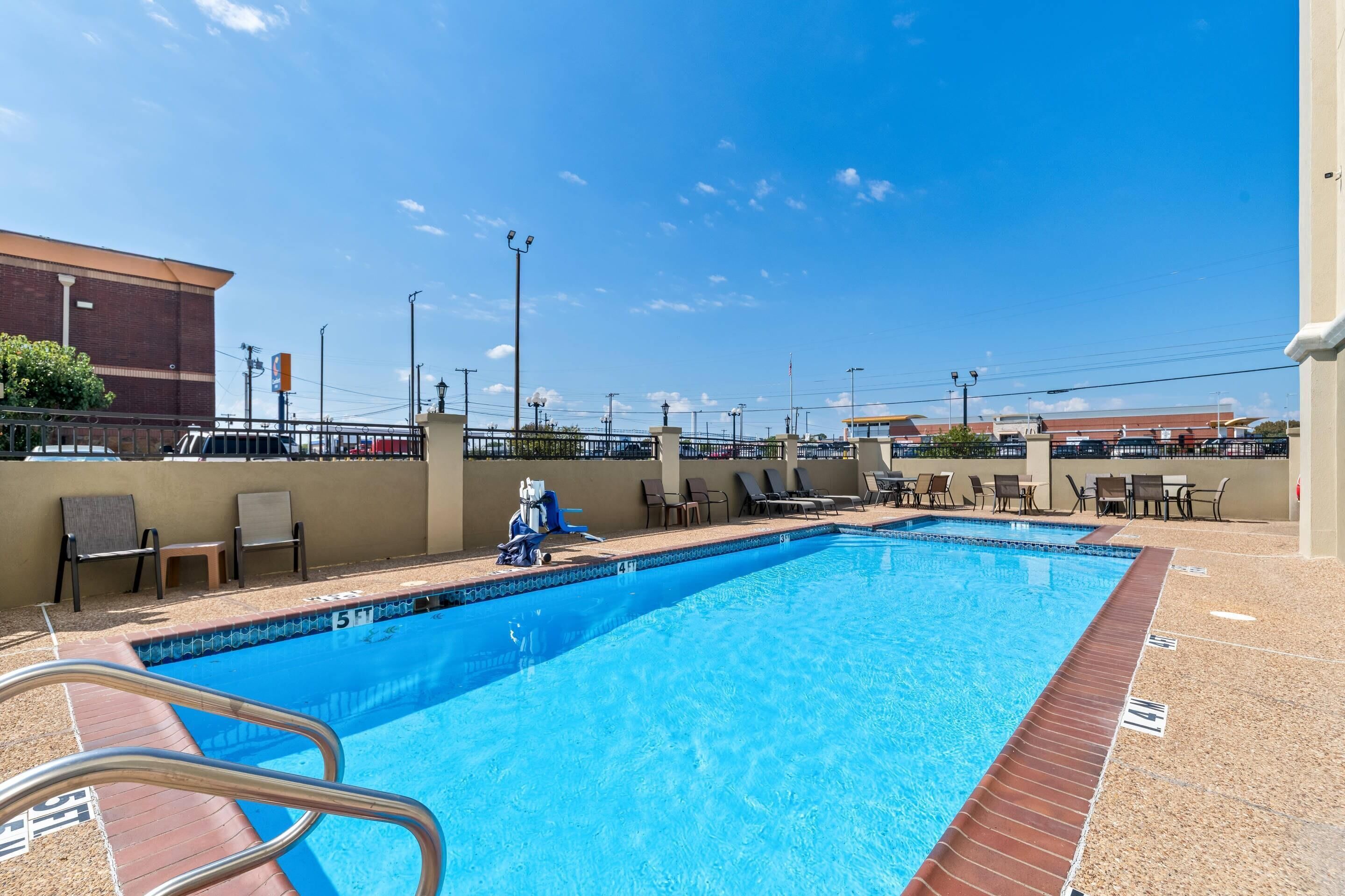 A swimming pool with a clear blue water, surrounded by lounge chairs and a brick wall.
