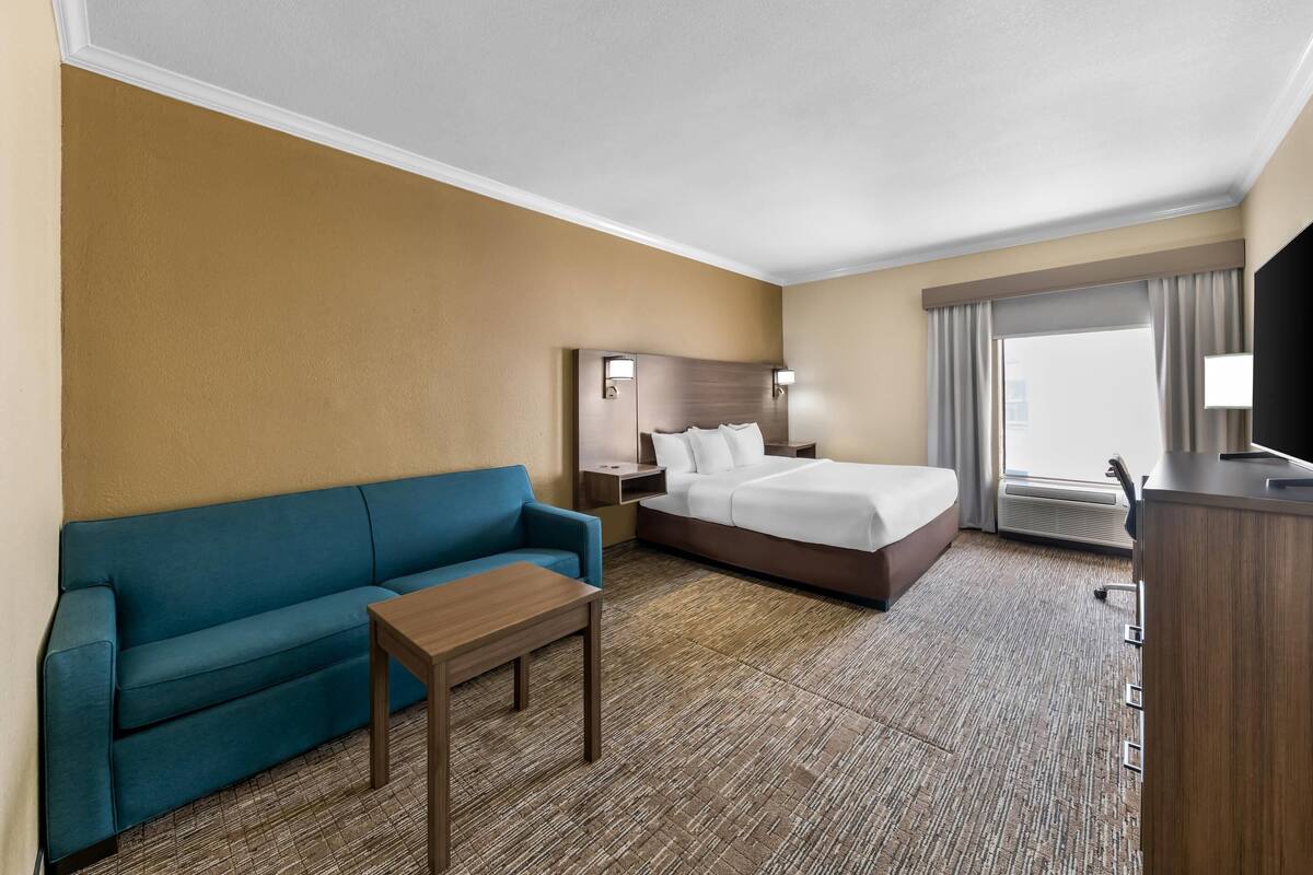 Ein Hotelzimmer mit einem Bett, einer blauen Couch, einem Holztisch und einem Fernseher.