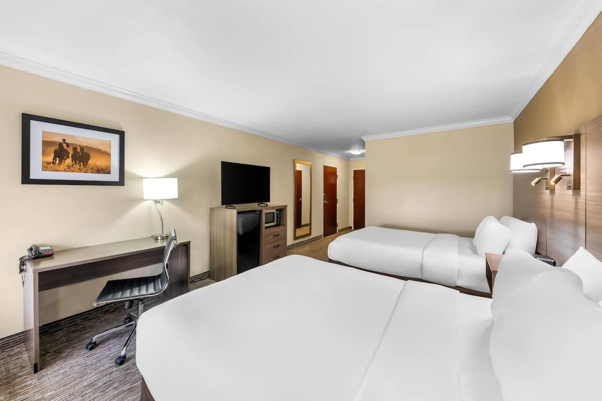 Ein Hotelzimmer mit Schreibtisch, zwei Betten, einem Fernseher und einem gerahmten Bild an der Wand.