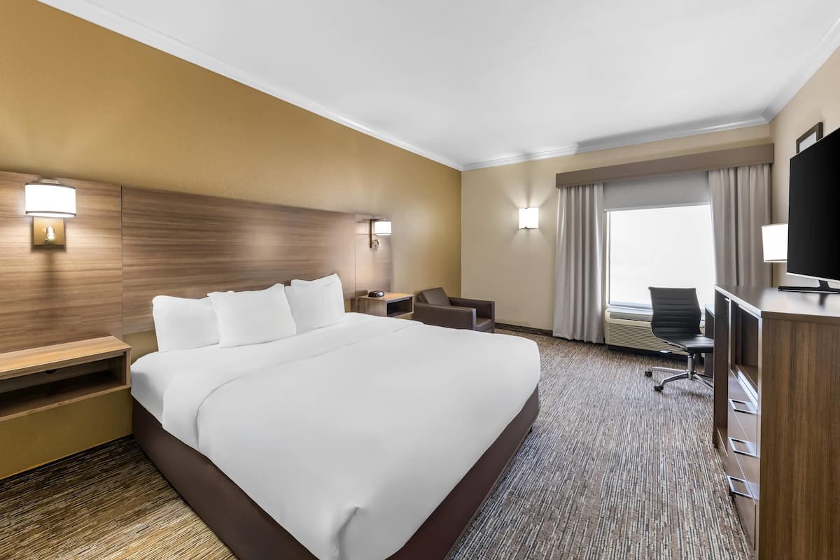 Ein Hotelzimmer mit einem großen Bett, Nachttischen, einem Schreibtisch mit Stuhl, einem Fernseher und einem Fenster mit Vorhängen.