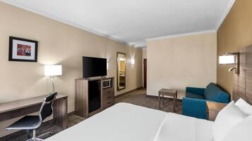 Una habitación de hotel con una cama, un escritorio con una silla, un televisor, una mesita pequeña y un sofá azul.