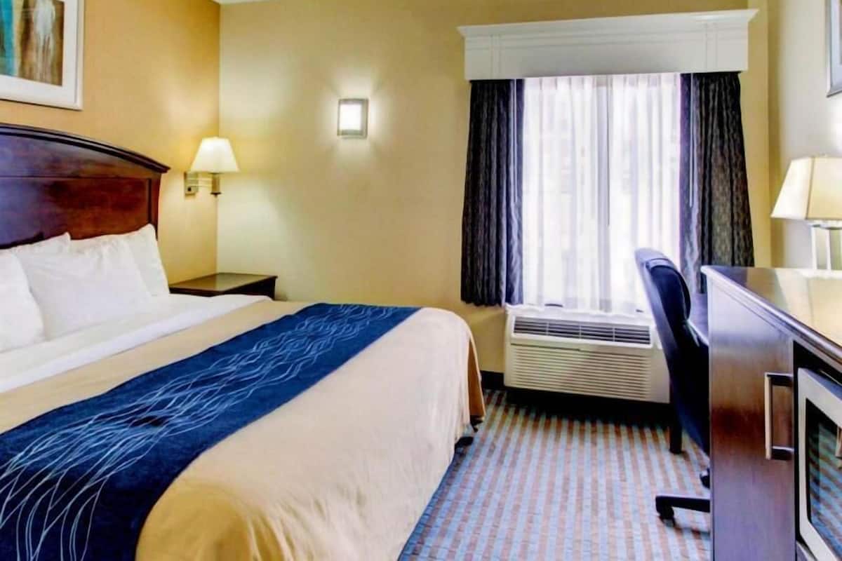 Ein Hotelzimmer mit Bett, Nachttischen, einem Schreibtisch, einer Klimaanlage und einem Fenster mit Vorhängen.