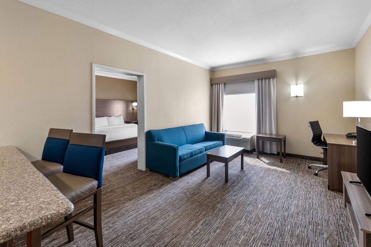 Ein Hotelzimmer mit einem Bett, einem blauen Sofa, einem Couchtisch, einem Schreibtisch mit Computer und einem Fernseher.