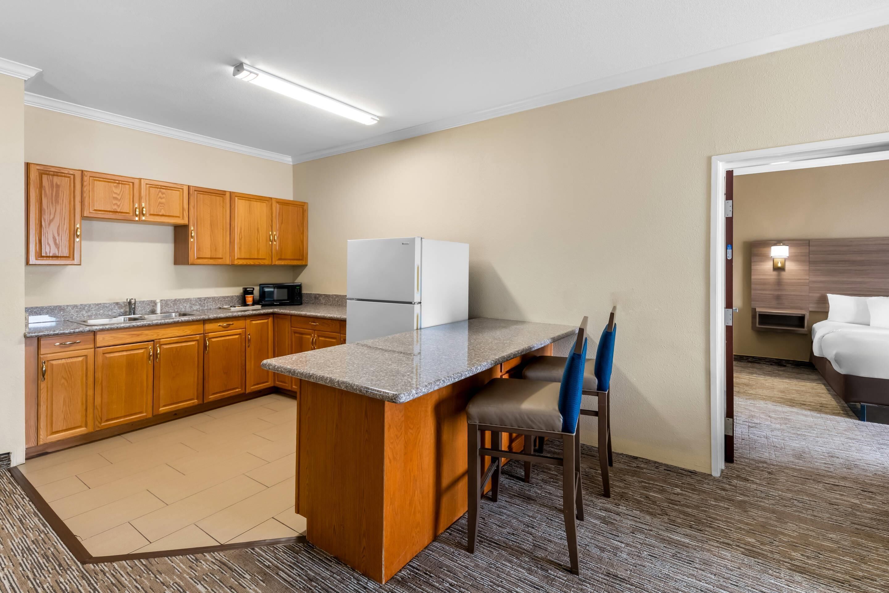 A compact kitchen with wooden cabinets, a refrigerator, a microwave, and a small island with bar stools.