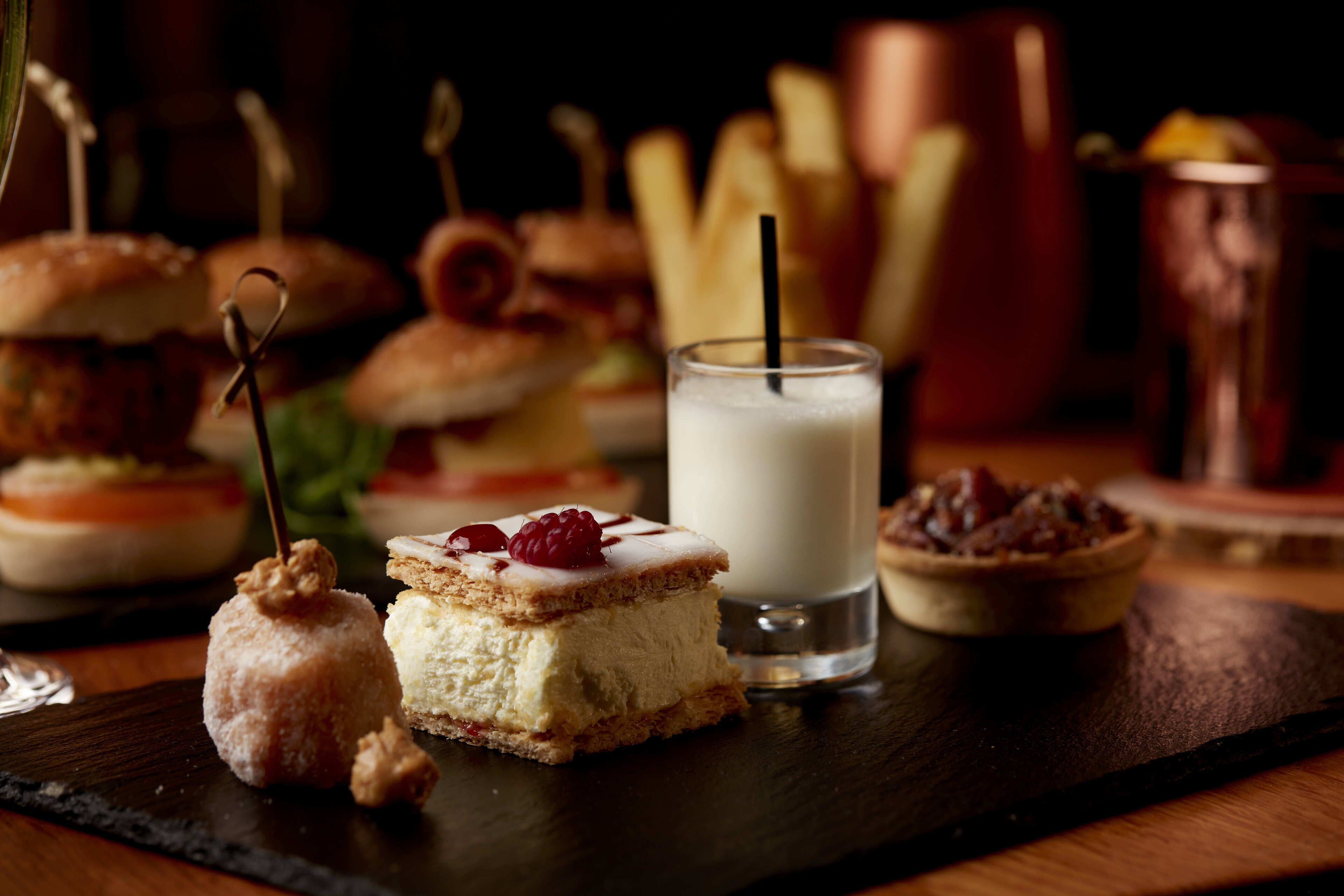 A dessert platter with various sweets and a glass of milk on a wooden table.