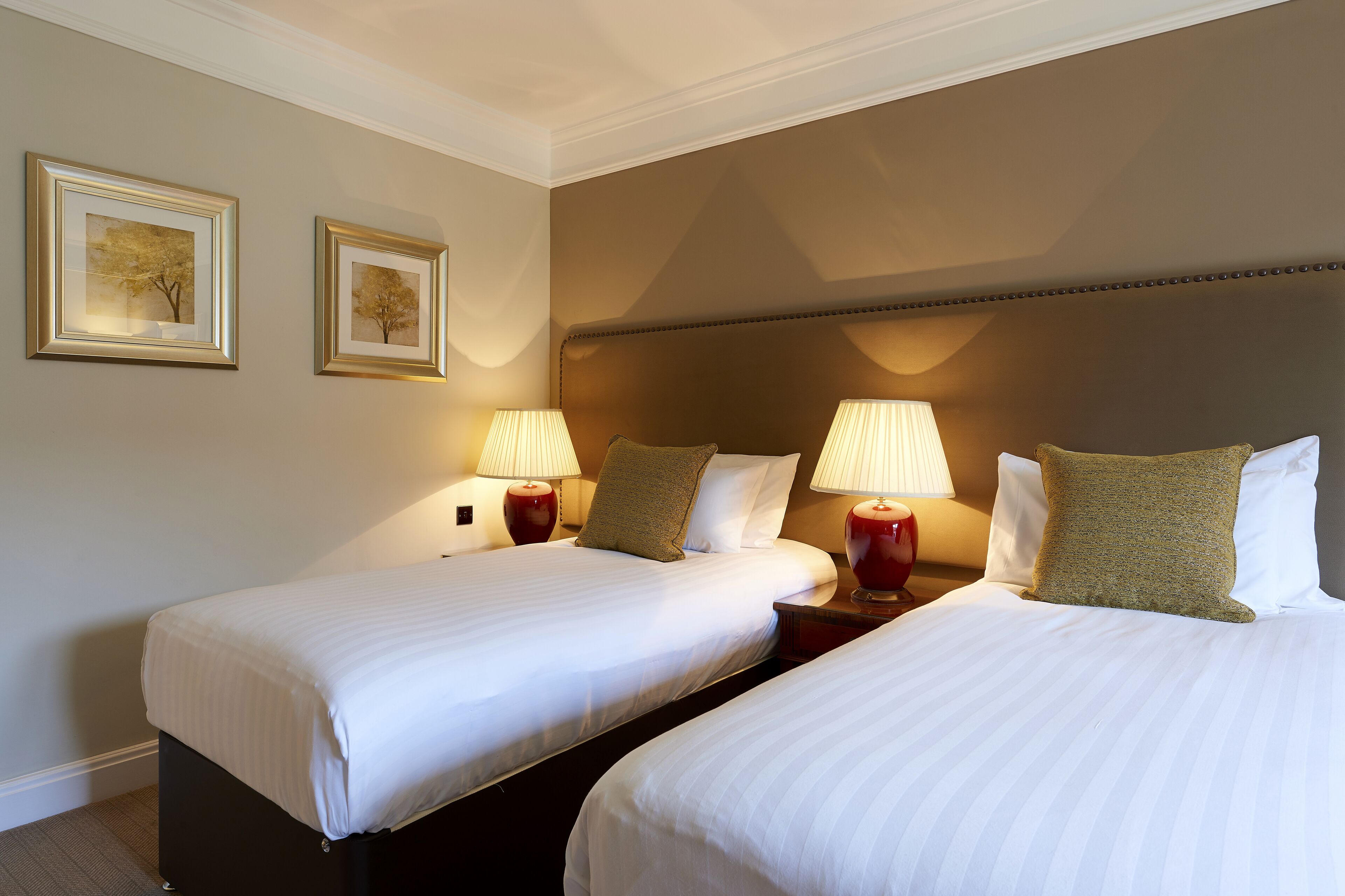 Una habitación de hotel con dos camas individuales, cada una con una lámpara y un almohadón.