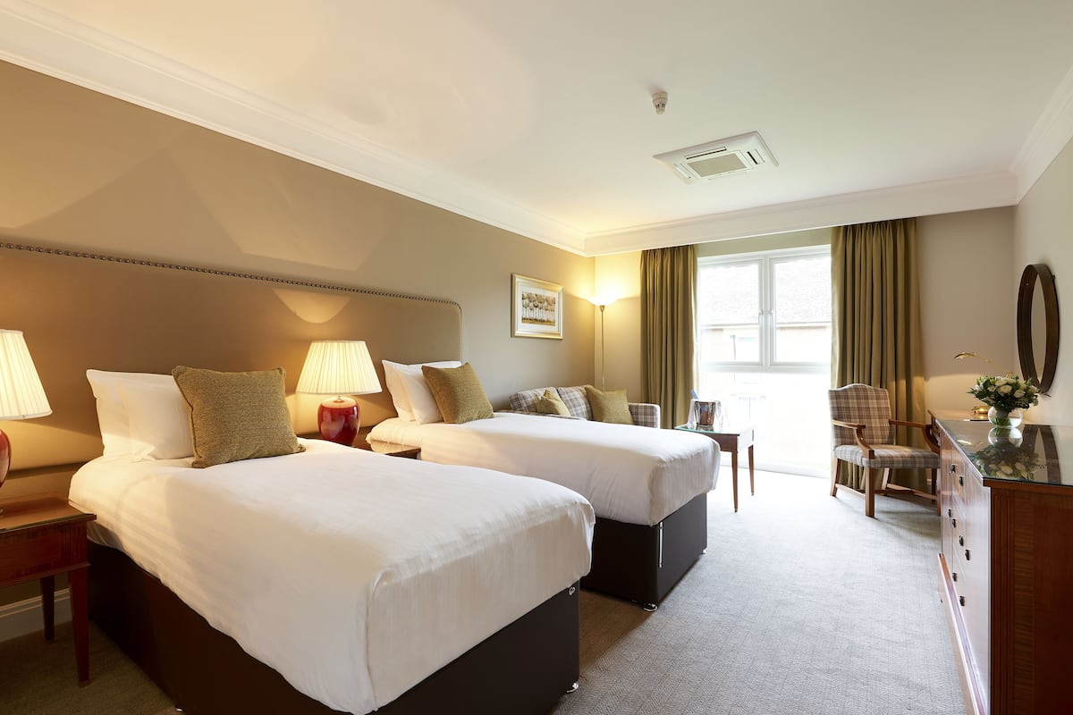A hotel room with two beds, a desk, a chair, and a dresser.