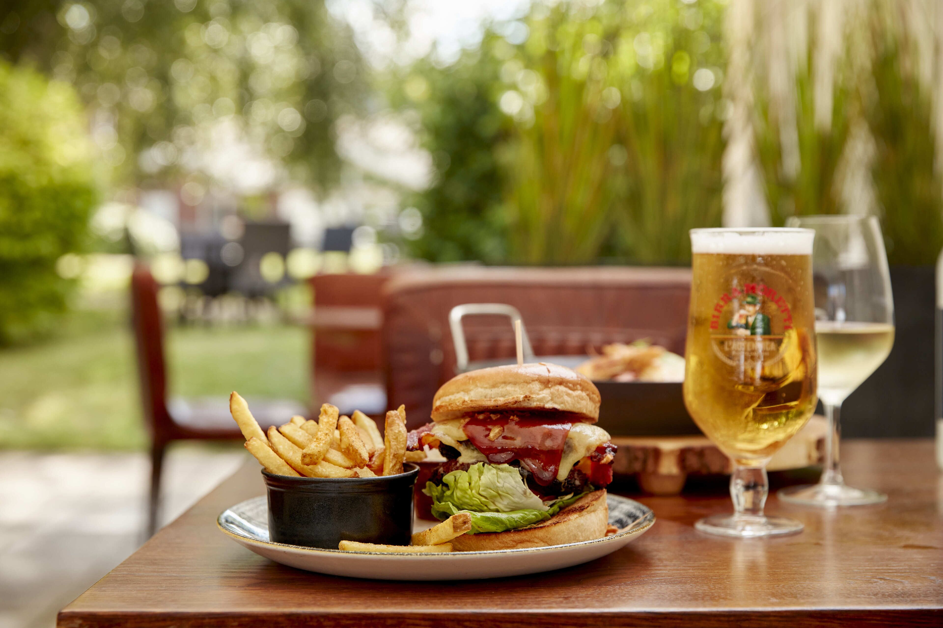 Una comida con una hamburguesa, papas fritas y una cerveza sobre una mesa de madera.