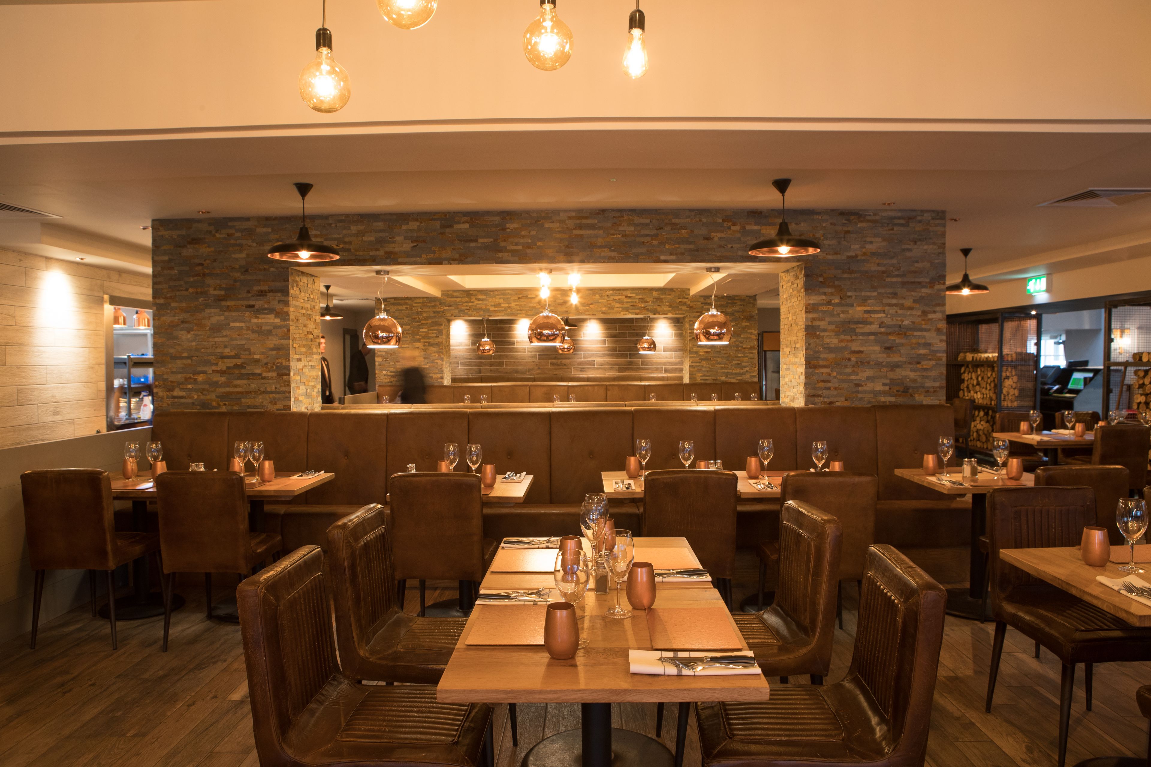 A restaurant with wooden tables and chairs, stone walls, and hanging pendant lights.
