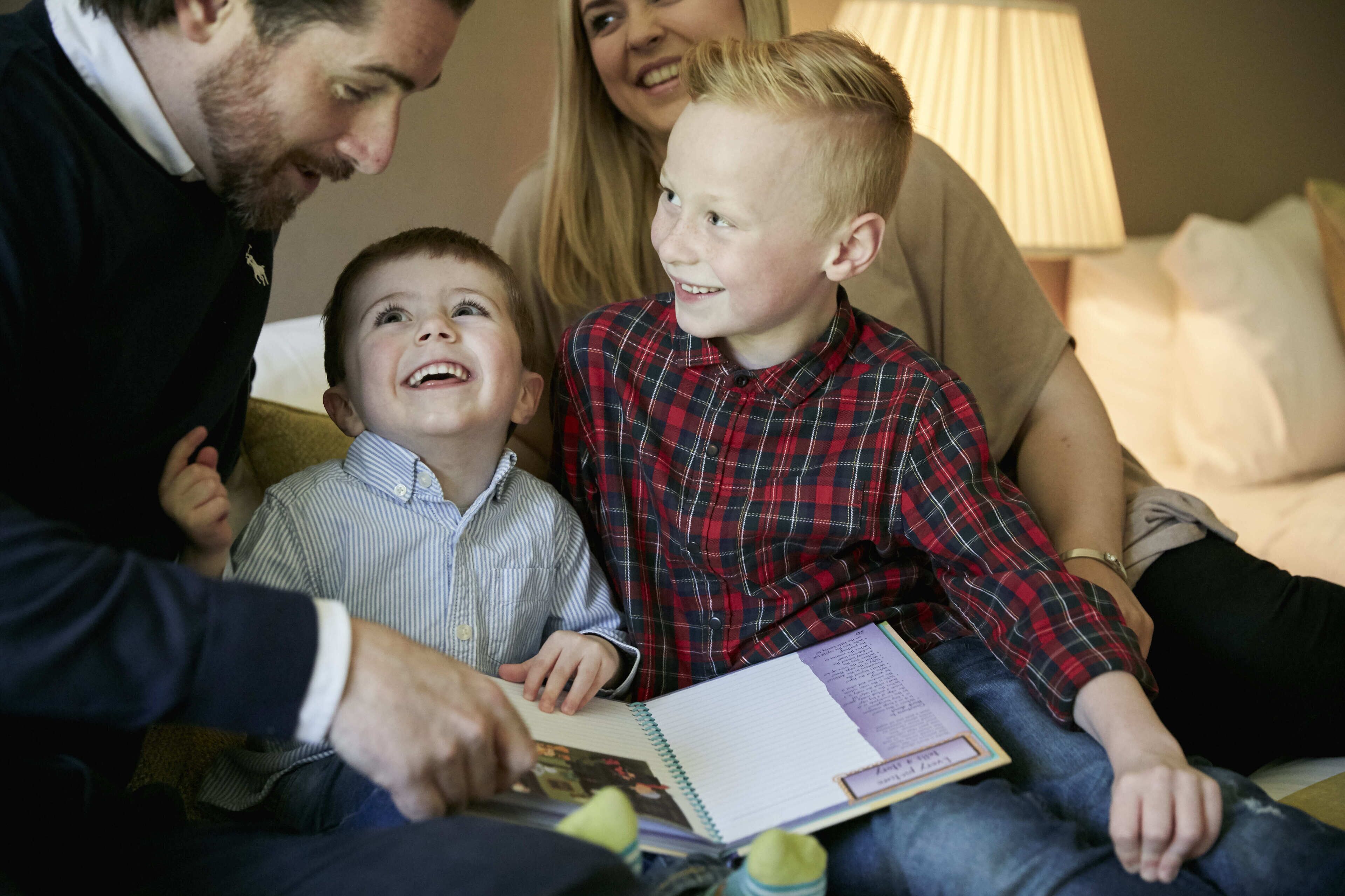 A family sitting on a couch with a book, a lamp, and a pillow in the background.