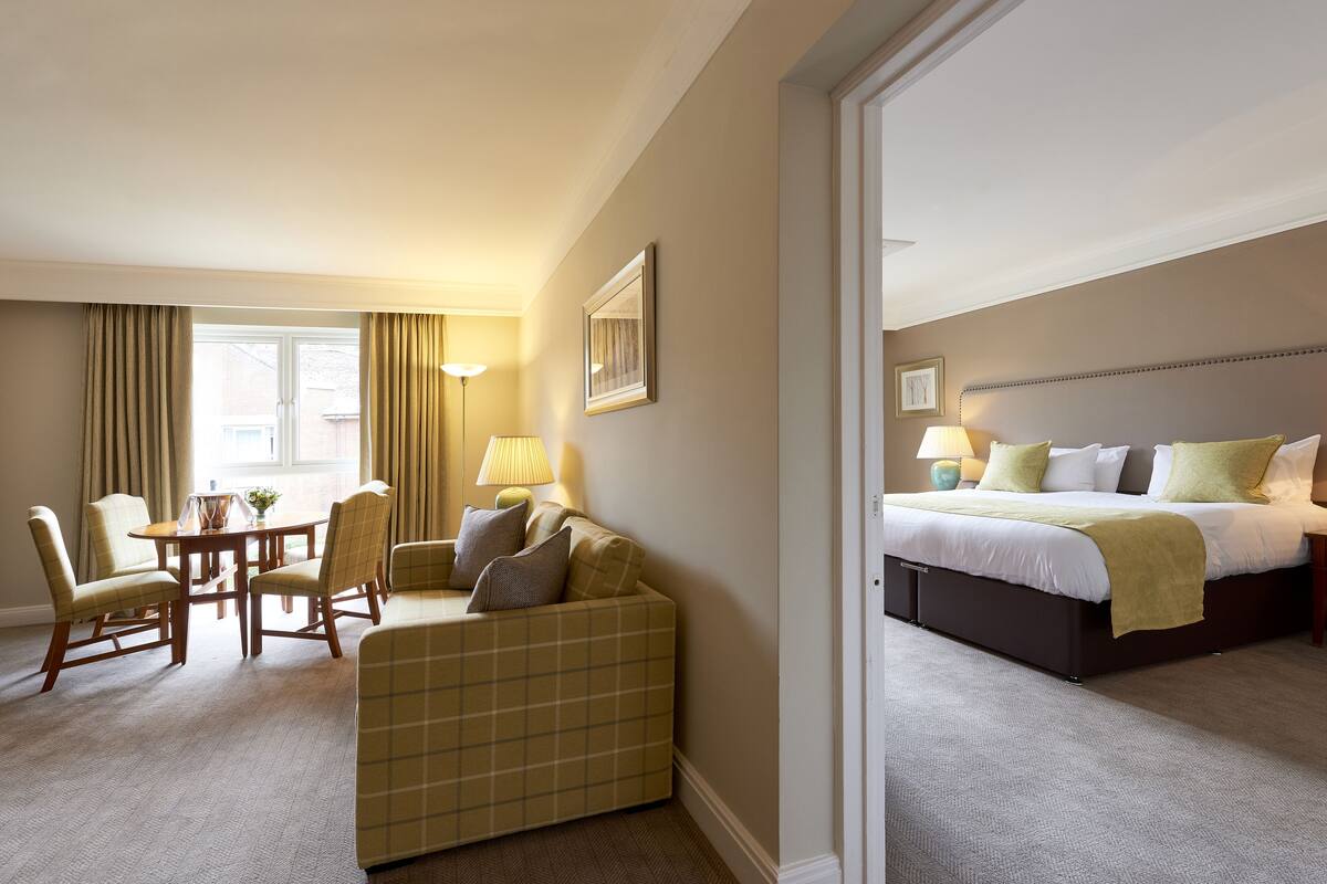 Ein Hotelzimmer mit Bett, einer Couch, einem Esstisch mit Stühlen und einer Lampe.